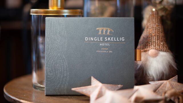 A Dingle Skellig Hotel brochure stands on a table beside glass jars, wooden stars, and a small decorative gnome with a knit hat.