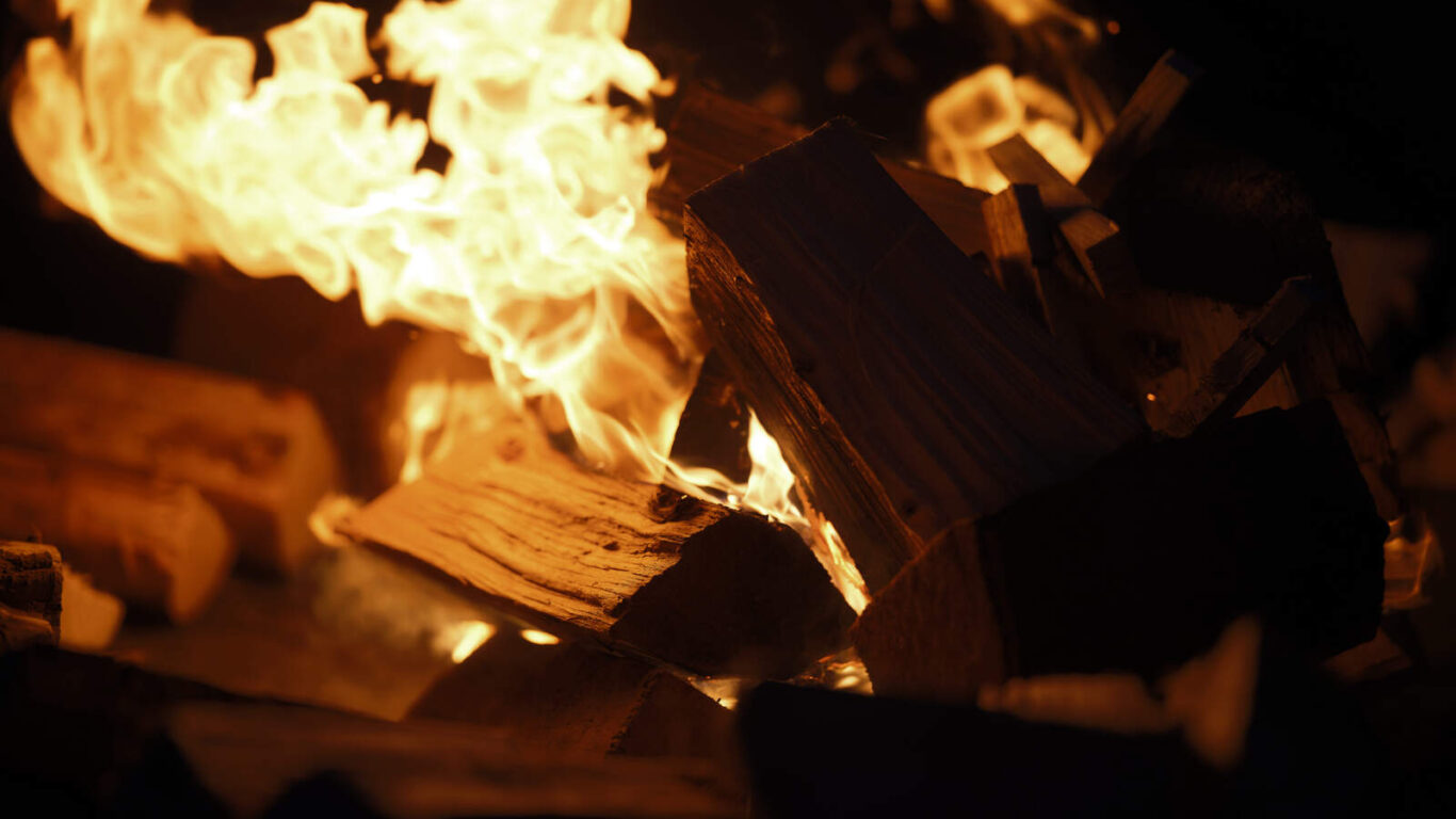 Close-up of burning firewood with bright orange flames in a dark setting.