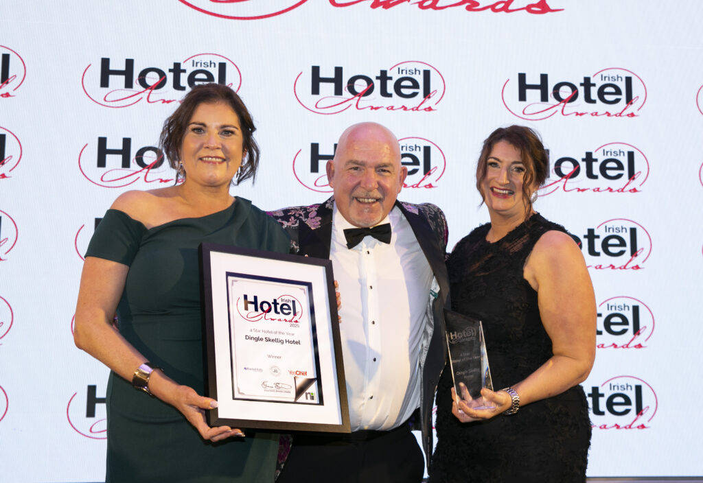 Three people pose at the Irish Hotel Awards event; one holds a framed certificate and another holds a glass trophy, with the event logo as the backdrop.