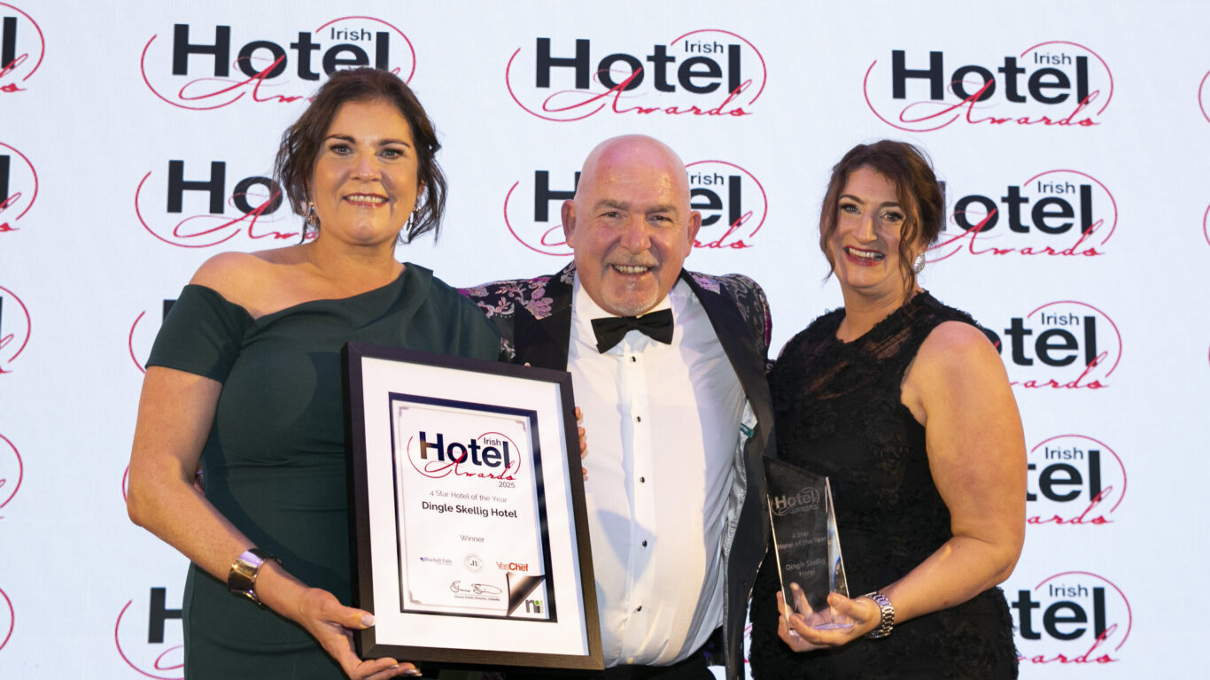 Three people pose at the Irish Hotel Awards event; one holds a framed certificate and another holds a glass trophy, with the event logo as the backdrop.
