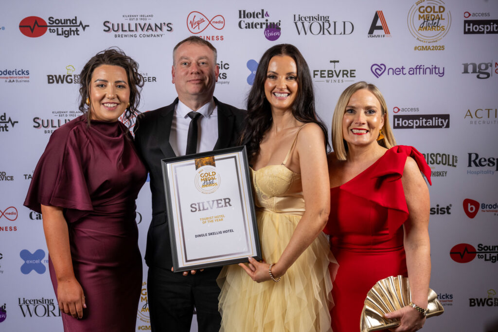 Four people dressed formally pose together, one holding a framed Silver award certificate, in front of a sponsor-branded backdrop at an awards event.