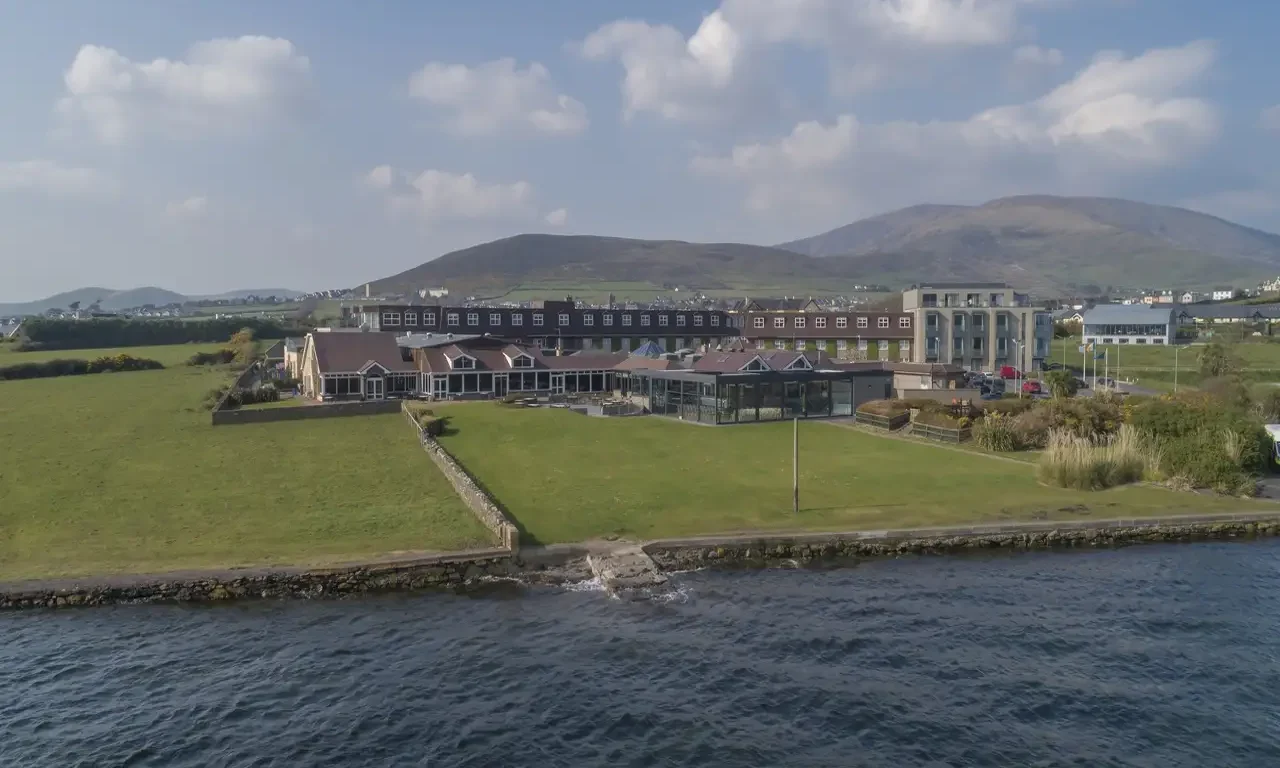 Coastal hotel with stunning sea views, lush green lawn, and nearby mountain backdrop, perfect for a relaxing stay.
