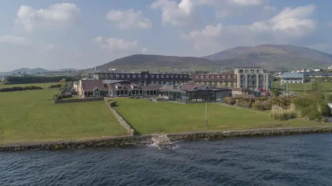 Coastal hotel with stunning sea views, lush green lawn, and nearby mountain backdrop, perfect for a relaxing stay.